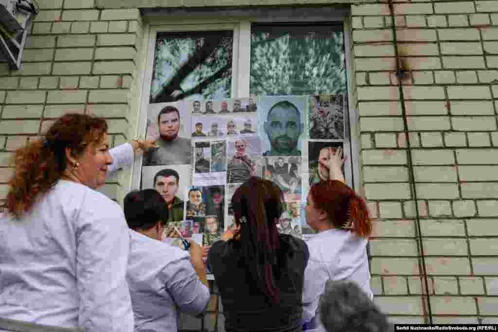 Рідні полонених кріплять фото своїх близьких, які в полоні, на імпровізований стенд, щоб звільнені захисники могли подивитись і якщо когось впізнають, розповісти хоч якусь інформацію