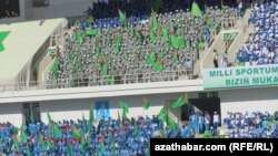 20 müň tomaşaçy üçin niýetlenen “Aşgabat” stadionynyň tribunalaryny dolduryp oturan studentler we edara işgärleri ýörite "režissýoryň" görkezmesi boýunça hereket edýärler. Aşgabat, 20-nji sentýabr, 2012.