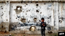 Сирийский ребенок с игрушечным оружием на фоне простреленной стены в пригороде Дамаска, 13 апреля 2017 