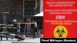 Люди на спортплощадке рядом с плакатом с информацией о профилактике COVID-19. Алматы, 12 июля 2020 года.