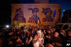 Прихильники Джордже Сіміона реагують на результати екзитполів на тлі зображень румунських історичних постатей біля штаб-квартири Альянсу за об’єднання румунів (AUR) після закриття виборчих дільниць у першому турі повторних президентських виборів у Бухаресті, 4 травня 2025 року