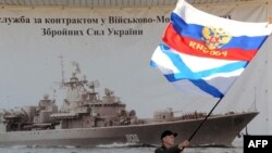 Ukraine -- A man waves a Russian flag and a Russian Navy flag in front of the headquarters of the Ukrainian Navy in Sevastopol on March 3, 2014.