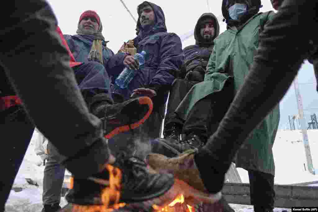 Migrants warm their feet by a fire at the camp.