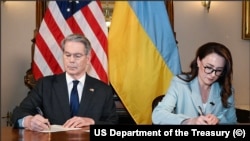 اسکات بسنت (چپ)، وزیر خزانه‌داری ایالات متحده و یولیا سویردنکو، وزیر اقتصاد و معاون نخست‌وزیر اوکراین در حال امضای قرارداد مواد معدنی کمیاب