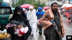 An Afghan woman walks through a market as a Taliban fighter stands guard in Kabul. (file photo)