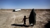 یک زن روستایی و فرزندش در حال گذار از تالاب خشکیده هامون در نزدیکی روستای سیخ‌سر در حوالی زابل