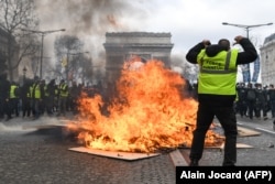 Учасник руху «Жовті жилети» жестикулює за полум’ям, що піднімається з барикади. Париж, Франція, 16 березня 2019 року