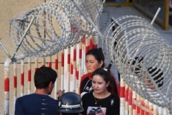 Aýallar Hotan şäheriniň bazarynyň girelgesindäki tikenli simleriň öňünde. Hytaýyň Şinjiang welaýaty. 2019-njy ýylyň 31-nji maýy.