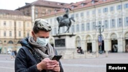 Көчөдө телефонун тиктеп бараткан аял. Иллюстрациялык сүрөт. Италиянын Турин шаарында тартылган.