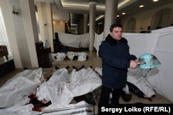 Володимир Голоднюк тримає шолом свого сина Устима Голоднюка. У шоломі кульовий отвір. На підлозі у холі готелю «Україна», пристосованому під морг, лежать тіла вбитих майданівців. Голоднюк щойно впізнав серед них свого сина. Фото Сергія Лойка. Київ, 20 лютого 2014 року