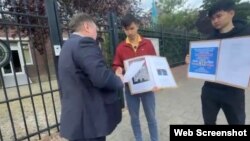 Кымбат Абеуулы (в центре) и Таскын Кудайберген разговаривают с представителем посольства во время акции протеста у здания посольства Казахстана в Амстердаме. 25 августа 2025 года. Скрин видео