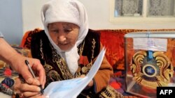 Женщине помогают поставить отметку в избирательном бюллетене в день голосования на досрочных выборах президента Казахстана. Алматинская область, 3 апреля 2011 года.