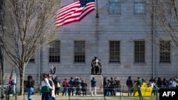 Protestatari cu placate adunați în fața statuii lui John Harvard în Harvard Yard, în urma unei demonstrații, pe 17 aprilie 2025.