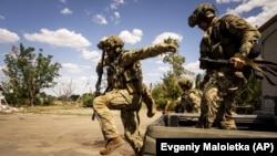 Українські військовослужбовці вистрибують з кузова автомобіля, щоб зайняти позицію на передовій в Миколаївській області, 8 серпня 2022 року