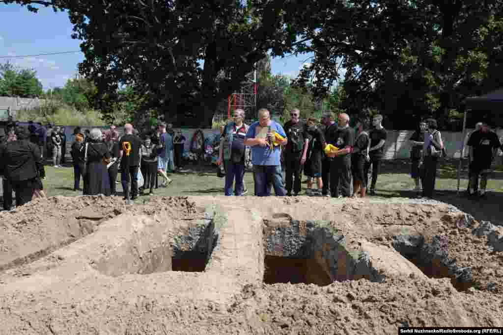 Батько і чоловік Дмитро стоїть з портретами своїх близьких біля могил