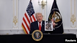 ترامپ عکس معروفی را در دست دارد که ازدحام افغان‌های فراری در زمان تصرف کابل به دست طالبان در یک هواپیمای باری را نشان می‌دهد