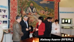 Посетители выставки «Мир Абая» осматривают экспозицию. Cлева направо: главный редактор газеты «Қазақ әдебиеті» Жумабай Шаштайсулы, директор института «Абай» Казахского национального университета имени аль-Фараби Жанкара Дадебаев, ученый секретарь областного историко-краеведческого музея города Семей Шынар Садыкова. На заднем плане — гобелен с портретом Абая, выполненный по эскизу Абылхана Кастеева. Алматы, 30  сентября 2015 года.