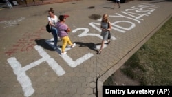 People walk along the inscription "We will not forget!" painted on the sidewalk near the place where Alyaksandr Taraykouski died amid the clashes during protests against the election results in Minsk in August 2020.