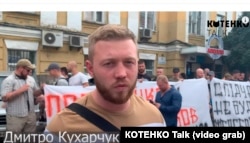 Скріншот з відео акції «Нацкорпусу» на підтримку Нікіти Макєєва. На передньому плані Дмитро Кухарчук, позаду з мобільним телефоном Сергій Коротких, за транспарантом над буквою «К» видно обличчя Тараса Стасівського