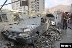 Израильдің әуе шабуылы салдарынан бүлінген көліктердің қасында тұрған адамдар. Тегеран, 13 маусым, 2025 жыл.