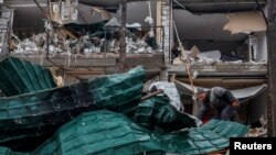 19-njy martda Ukrainanyň Kiýew sebitiniň Hostomel şäherinde rus pilotsyz uçarynyň zarba uran ýerinde zeper ýeten jaýlaryň harabalyklaryny arassalaýan adam.