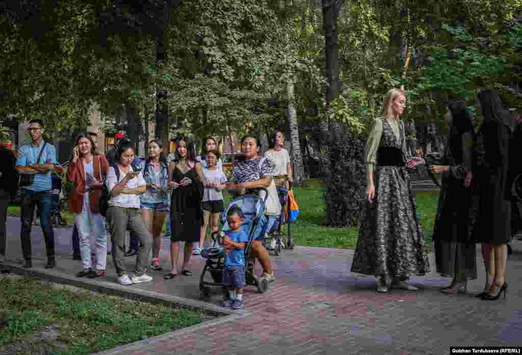 Моделдердин жанында турган көрүүчүлөр.