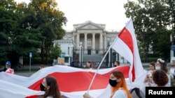 Людзі нясуць нацыянальны беларускі сьцяг падчас маршу салідарнасьці зь беларускім народам пасьля абвяшчэньня вынікаў прэзыдэнцкіх выбараў у Беларусі. Варшава, Польшча, 14 жніўня 2020 году