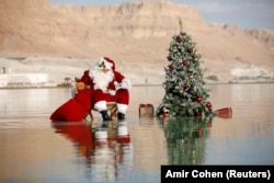 Баскетболчу Исса Кассиссие жомоктогу Санта-Клаустун кийимин кийип, Өлүк деңиздеги балатынын жанында сүрөткө түштү. Израилдик туризм министрлиги чет элдик туристтерди Ыйсанын туулган күнү жана Жаңы жыл майрамдарын белгилөө үчүн өз өлкөсүнө чакырып, ушул рекламалык сүрөттү даярдады. Эйн-Бокектин жаны. 2020-жылдын 15-ноябры.