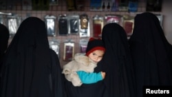 Qadın Al-Hol lageriniñ tükânında balasını quçağında tuta, Suriye. 2020 senesi yanvarniñ 8-i