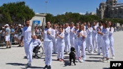 Ukrainian gymnast Mariya Vysochanska (second from left) holds the Olympic torch and lights the torch of French alpine skier Cyprien Sarrazin (left) in Marseille.