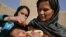 An Afghan woman holds a child as a health worker administers the polio vaccine. The WHO says that large-scale immunization can stop an outbreak.