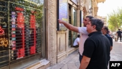 People look at currency exchange rates displayed on an electronic board on the window of a shop in in Ferdowsi Square in the Iranian capital Tehran on September 28.