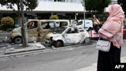 یک زن محجبه از خودروهایی که در اعتراضات فرانسه آتش گرفته‌اند عکس می‌گیرد؛ پنجشنبه هشتم تیر، حومه پاریس