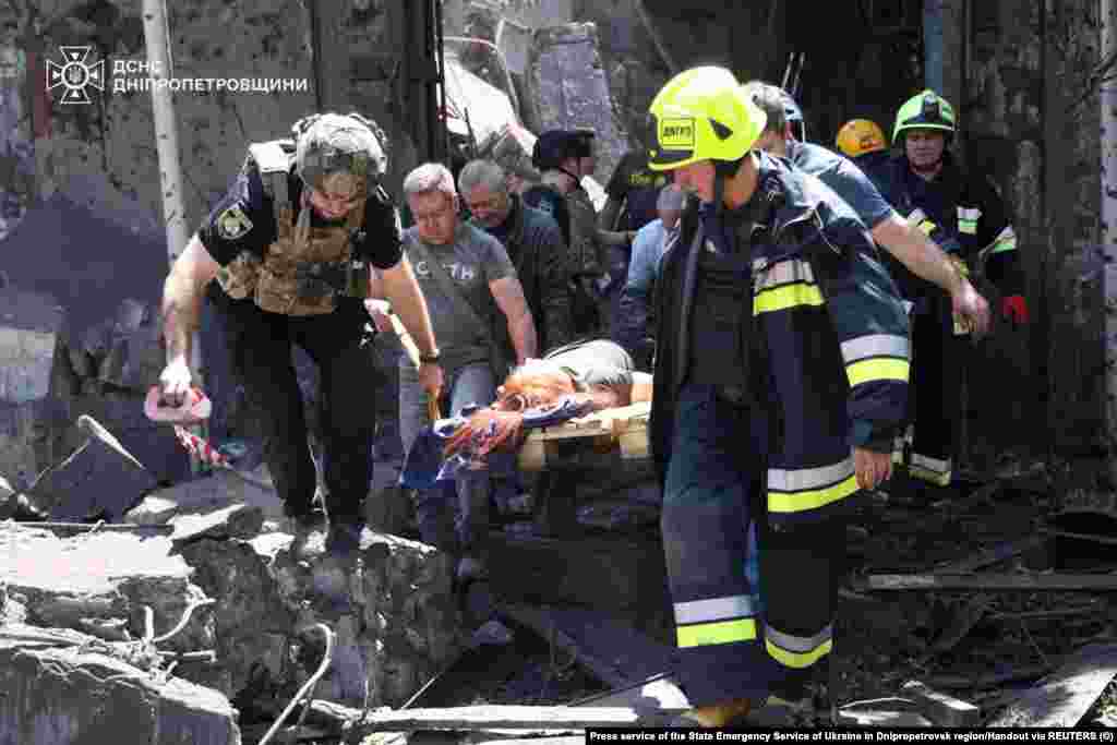 Рятувальники несуть поранену жінку, яку врятували з-під завалів будівлі, пошкодженої внаслідок російського ракетного удару 24 червня 2025 року.Наразі відомо про 18 загиблих людей через атаку РФ на Дніпро, двоє людей загинули в Самарі