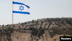 پرچمِ در اهتزاز اسرائیل، که بخشی از شهرک اسرائیلی معله آدومیم در کرانهٔ باختری در پس‌زمینه آن قابل مشاهده است