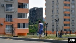 Жителька Маріуполя несе воду в бутлях улітку 2025 року. Відколи Росія окупувала місто, у ньому, як і в Донецьку після 2022 року, зникло нормальне водопостачання