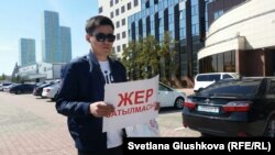 Жергілікті әкімдік алдында "Жер сатылмасын" деген плакат  ұстап тұрған адам. Көрнекі сурет.