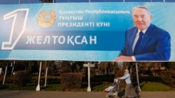 Женщина с ребенком проходит под баннером с изображением Нурсултана Назарбаева, установленным перед Днем первого президента Казахстана. Алматы, 30 ноября 2015 года