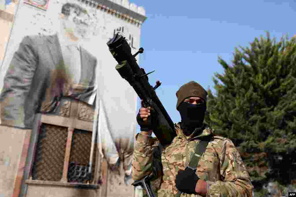 یکی از افراد ضدحکومتی با اسلحه در کنار یک دیوارنگاره آسیب&zwnj;دیده از بشار اسد در شهر حماه دیده می&zwnj;شود. این تصویر روز جمعه ۱۶ آذر ۱۴۰۳، پس از تصرف این شهر توسط نیروهای مخالف، ثبت شده است.