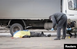 Police and forensic experts work next to the body of a victim covered by a Ukrainian national flag at the site of an attack on a Peace March in Kharkiv on February 22 that killed four peoople.