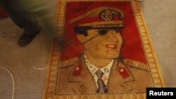 چهره معمر قذافی رهبر لیبی روی فرشی زیر پای معترضان در شهر بنغازی در سال ۲۰۱۱ 