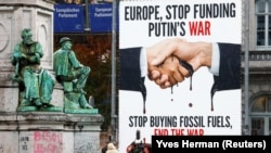 Активисты и представители СМИ возле открытого билборда с надписью "Европа, прекрати финансирование войны Путина. Прекратите покупать ископаемое топливо, завершите войну" у Европейского парламента в Брюсселе
