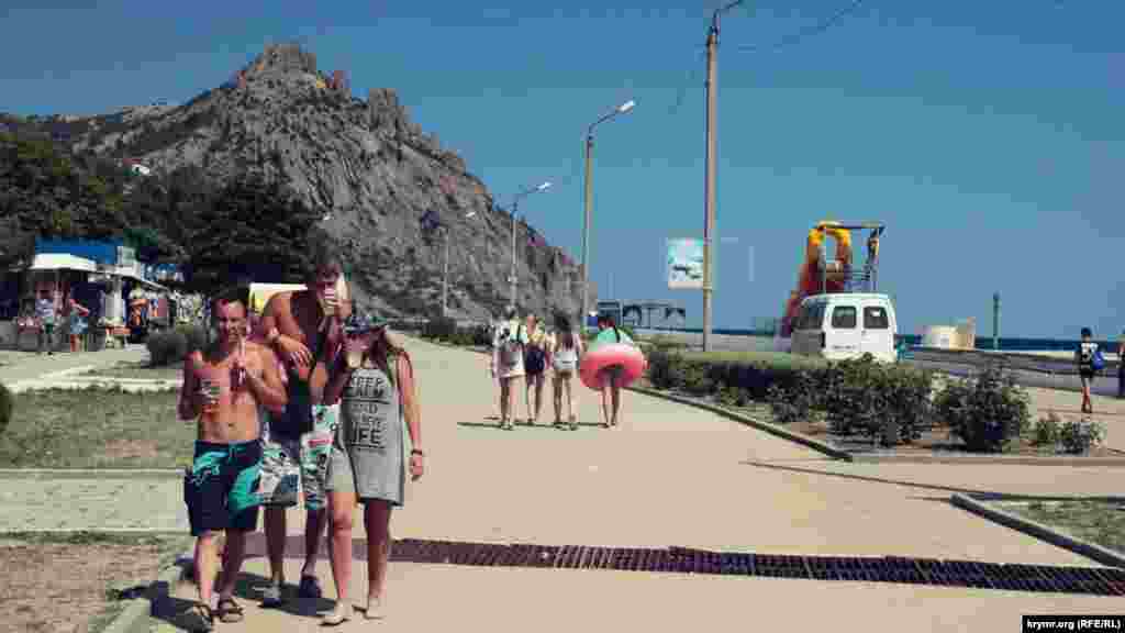 Отдыхающие прогуливаются по набережной и пьют пиво. На горизонте гора Кара-Даг