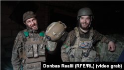 Військовослужбовець з позивним «Грім» демонструє свою каску, в яку влучила російська куля. Поруч боєць із позивним «Мєлкий»