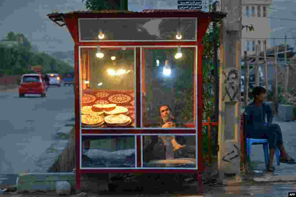 یک فروشنده افغان که نان می‌فروشد، در کنار خیابانی در منطقهٔ فیض‌آباد، ولایت بدخشان، منتظر مشتری است