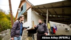 Жартысы қирап, бір жағына жантайып қалған үйінің жанында Дмитрий Абжан Азаттық тілшісі Том Бэлмфортпен әңгімелесіп тұр.  