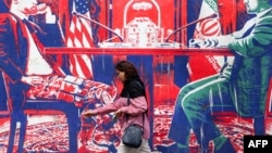 A woman walks past a mural depicting an Iranian official in civilian clothing sitting across the table from an American official wearing military fatigues painted on the outer walls of the former US Embassy in Tehran.