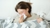A young woman lies in bed under a blanket and blows her nose in a napkin.Seasonal cold or flu concept 