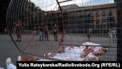 Хлопці та дівчата, одягнуті в біле, лежать на асфальті під «закривавленим» котком з металевих ґрат