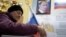 Женщина опускает бюллетень в урну на избирательном участке, где на стене висит портрет президента России Владимира Путина. Москва, 18 сентября 2016 года.